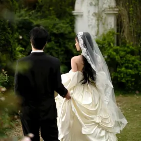 Bride and groom walking away through a garden, seen from behind