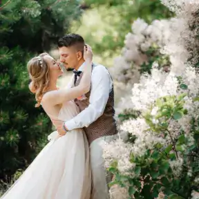 Couple embracing outdoors among white flowering bushes on their wedding day